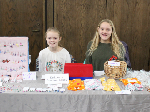 Two young girls selling crafts at a table