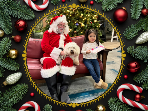 Little girl holding a book next to Santa and her dog